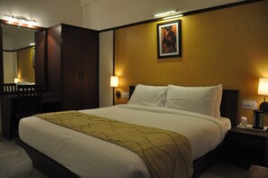 Une chambre d’hôtel avec un grand lit, une armoire, une table de chevet avec une lampe et un tableau encadré au mur.