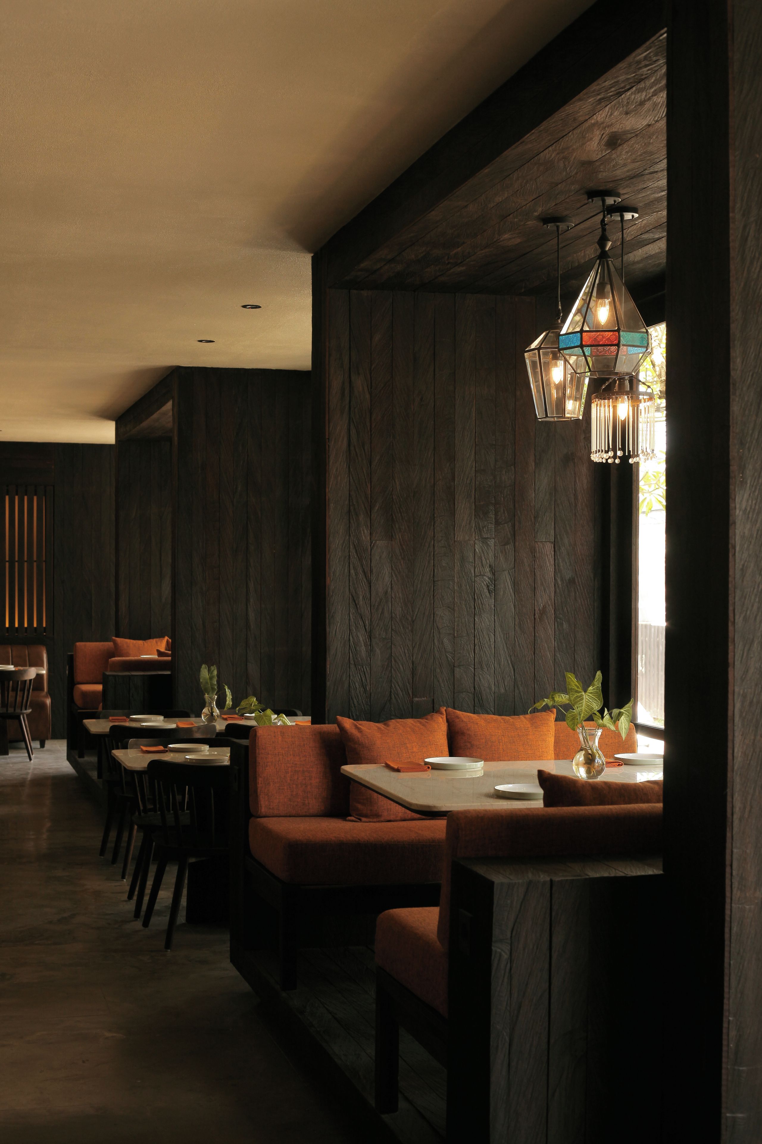 A modern interior with a wooden wall, a dining area with a sofa and tables, and a hanging light fixture.