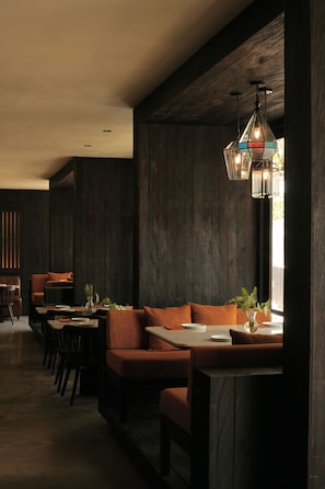 A modern interior with a wooden wall, a dining area with a sofa and tables, and a hanging light fixture. - Sapodilla Ubud (Ubud)