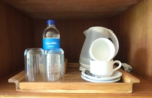 A wooden shelf with a water bottle, two glass jars, and a white cup and saucer.