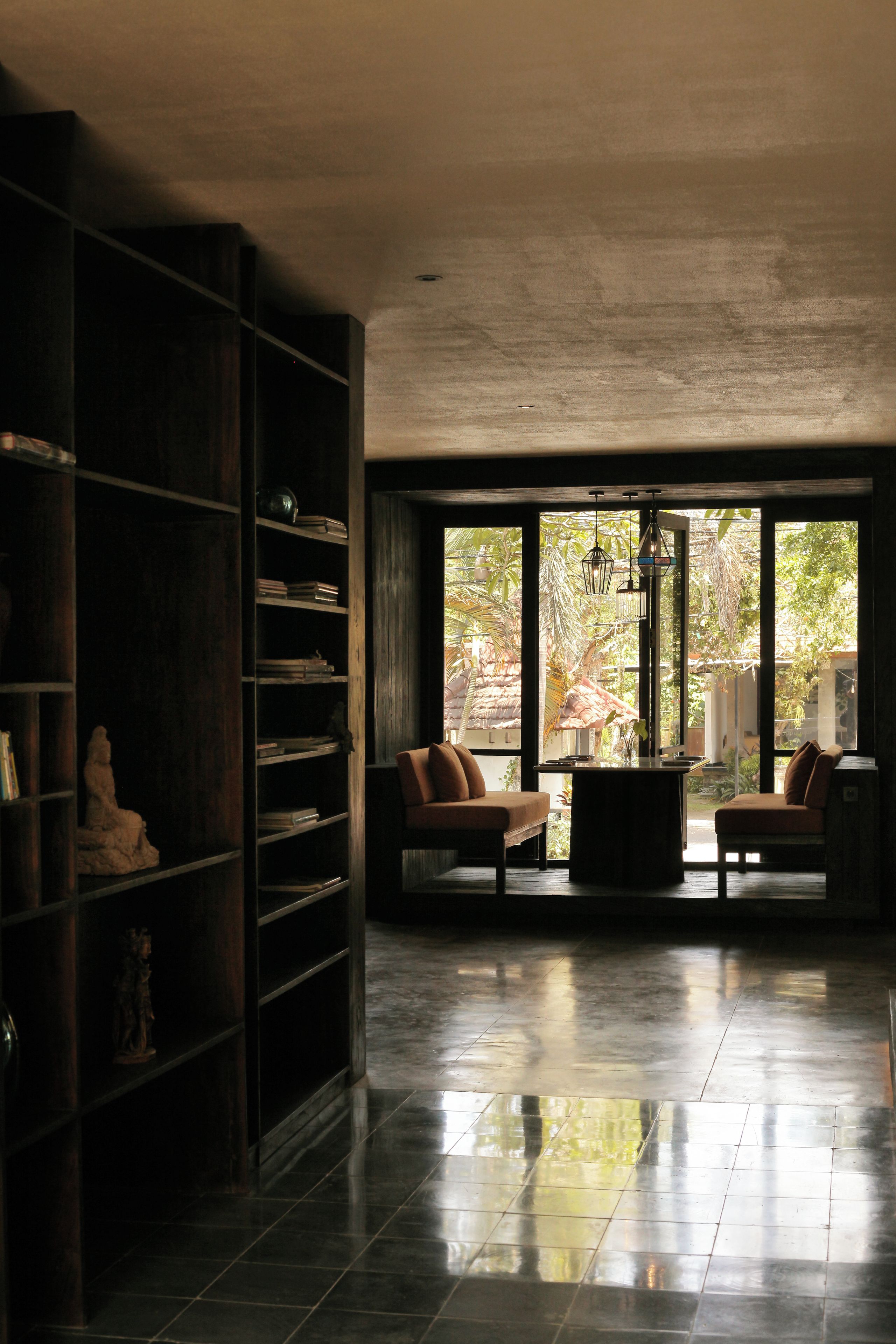 A spacious room with a large bookshelf, two cushioned seating areas, and a view of greenery outside.