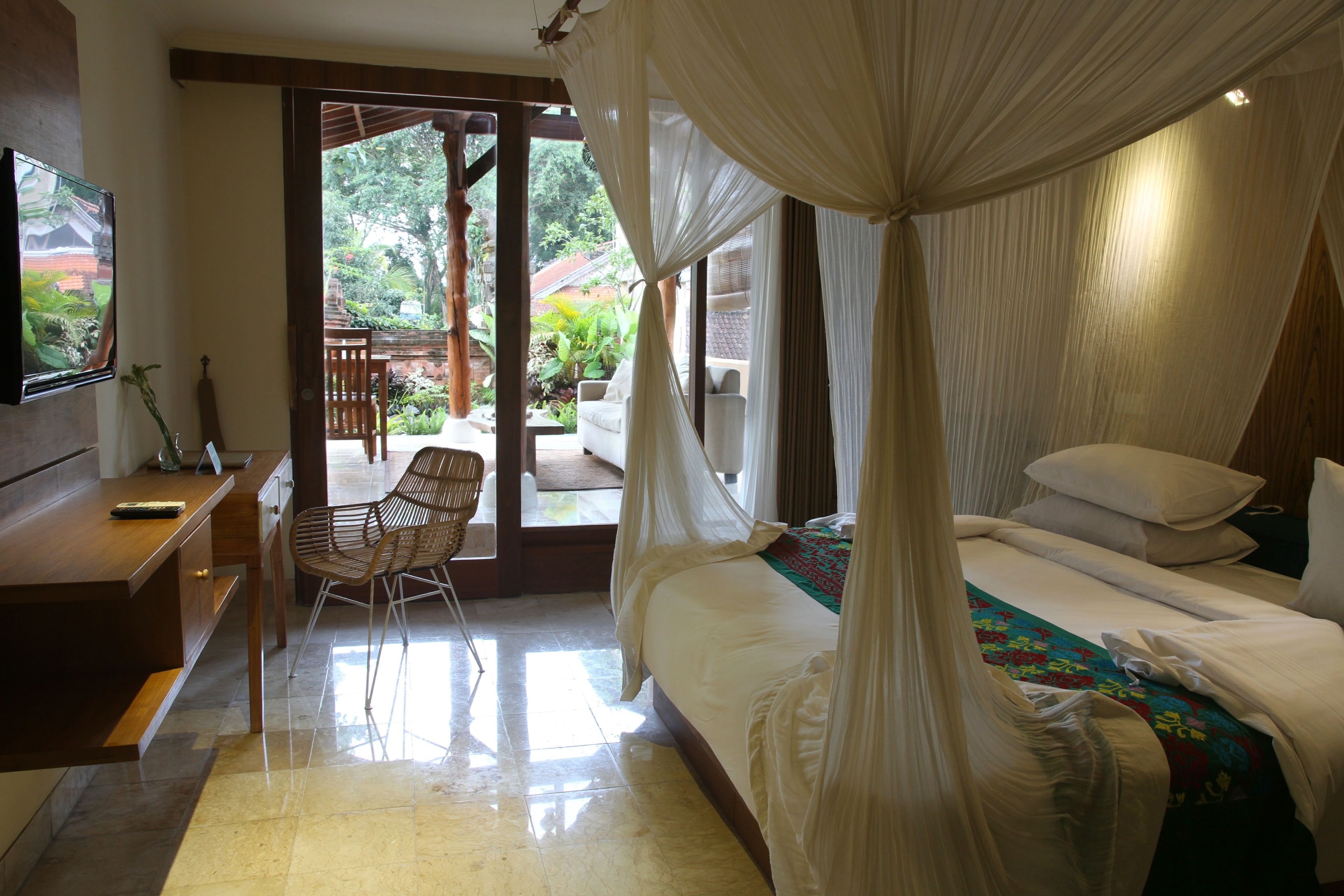 A bedroom with a bed, a desk, and a chair. There is a TV on the wall and a window with curtains.