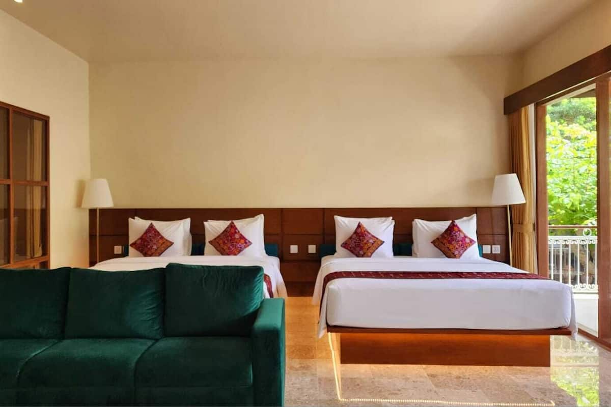 A hotel room with two beds, a green sofa, and a large window with a view of greenery.
