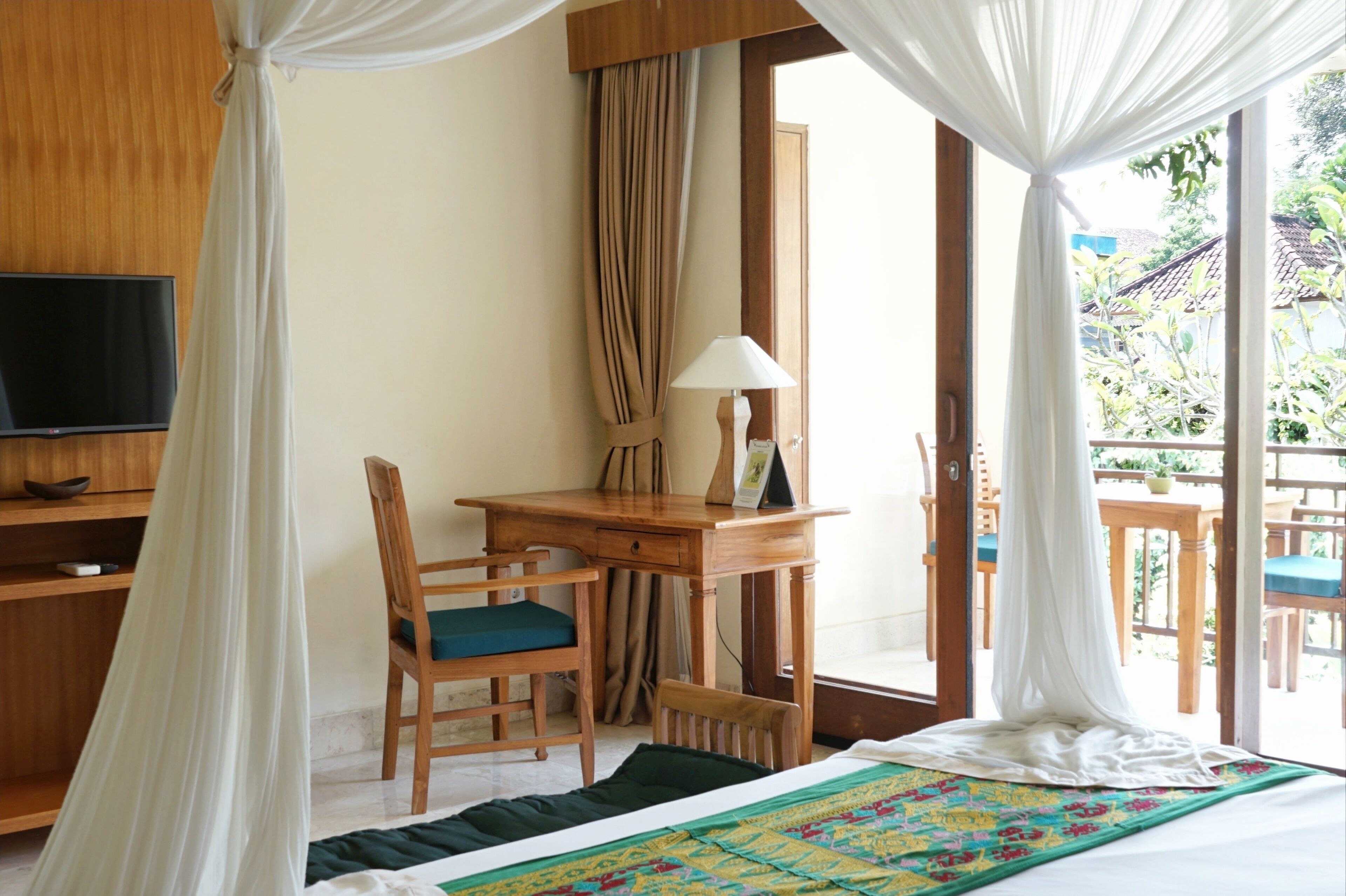 Una habitación con cama, escritorio, silla, televisión y vistas al exterior.
