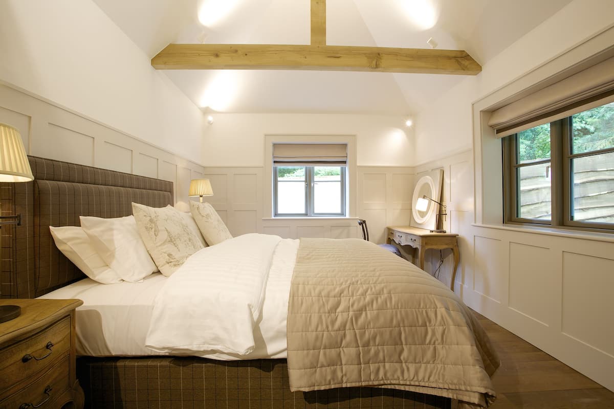 A bedroom with a large bed, a nightstand, a dresser, a window with a view, and wooden beams on the ceiling.