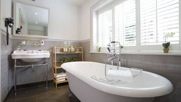 Ein modernes Badezimmer mit einer freistehenden Badewanne, einem Waschtisch mit Spiegel und einem Fenster mit Jalousien.