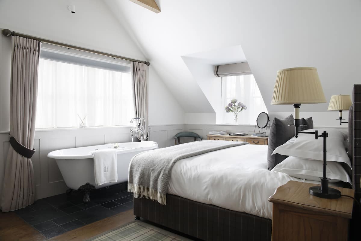 A modern bedroom with a large bed, a bathtub, a vanity with a mirror, and a desk with a lamp.