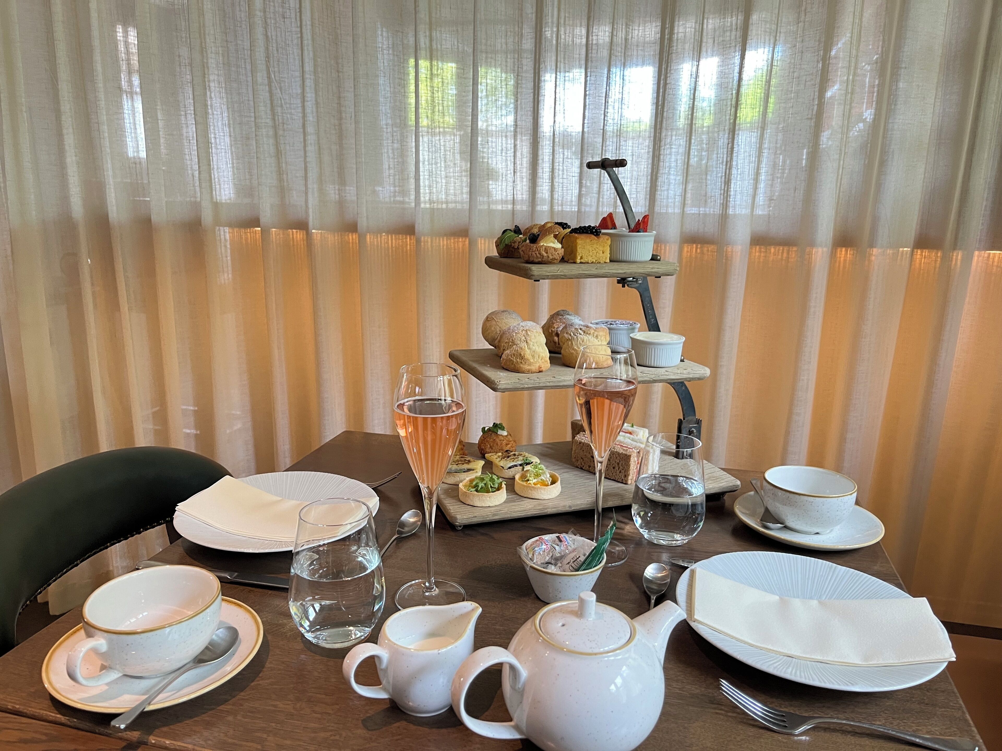 A table set for a meal with a tiered dessert stand, water glasses, a teapot, and plates.