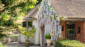 A house with a brick exterior, a tiled roof, and a hanging wisteria vine. There is a potted plant and a small garden area in front of the house. - Hurley House Hotel (Maidenhead)