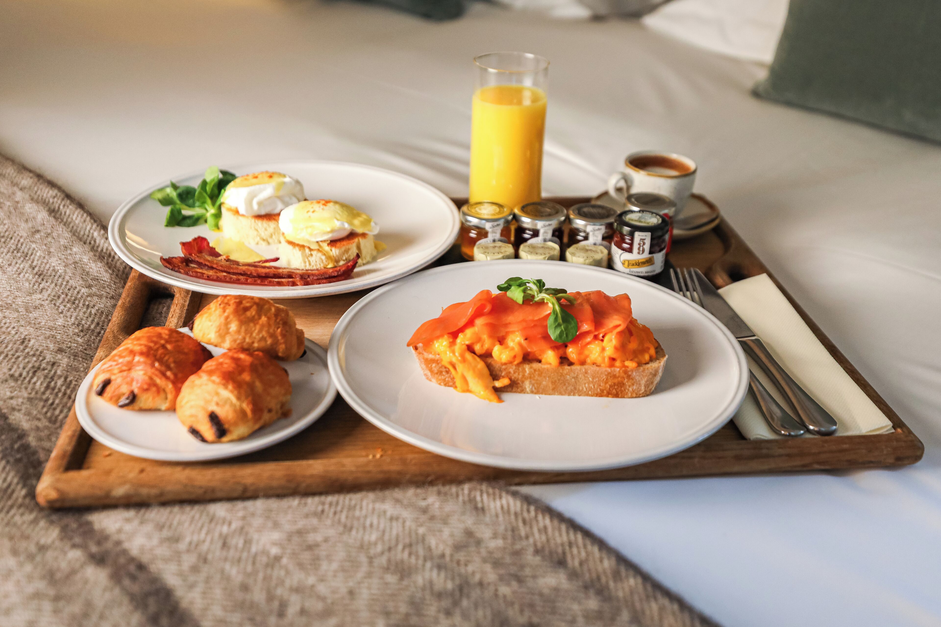 A breakfast tray with croissants, smoked salmon, and eggs on a bed.