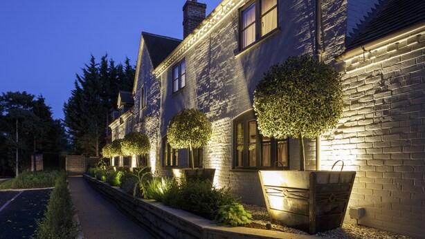 A stone building with multiple windows and a brick chimney, surrounded by a well-maintained garden with various plants and a pathway. - Hurley House Hotel (Maidenhead)