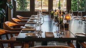 A dining table set with multiple wine glasses, plates, and cutlery, surrounded by leather chairs. - Hurley House Hotel (Maidenhead)