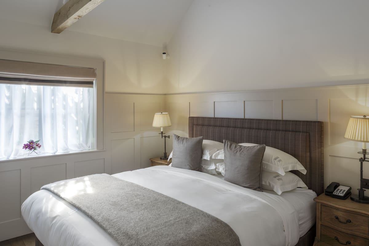 A neatly made bed with a grey throw blanket, a bedside lamp, and a telephone on a wooden nightstand.