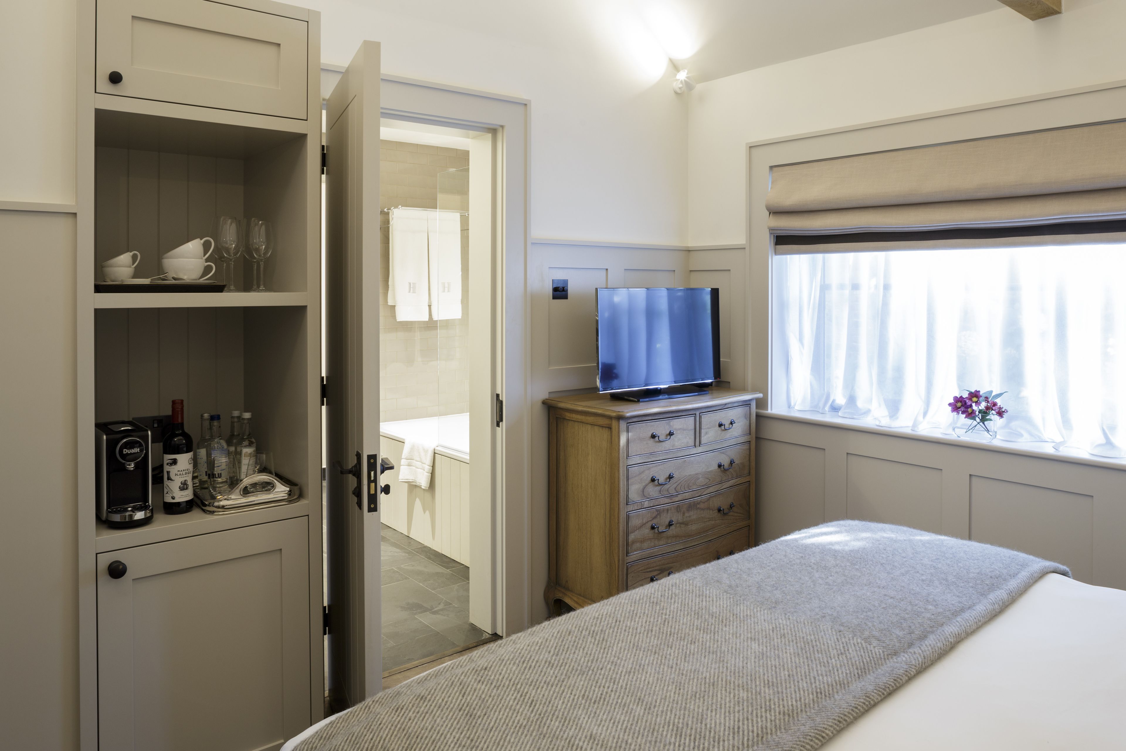 Un dormitorio con una cama, un televisor sobre un aparador de madera, un armario y un baño visible a través de una puerta abierta.