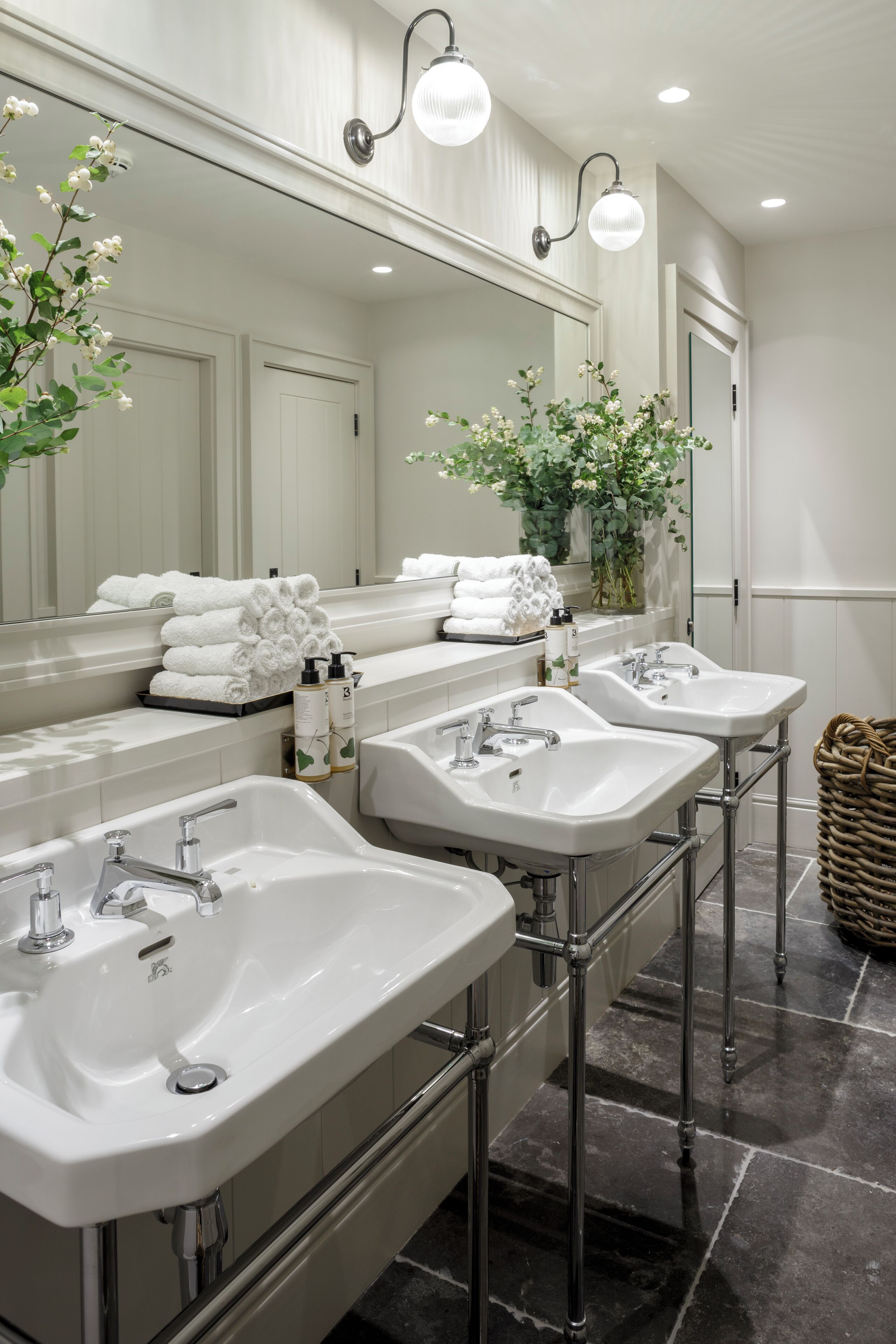 Une salle de bain moderne avec trois lavabos, un grand miroir et des plantes décoratives.