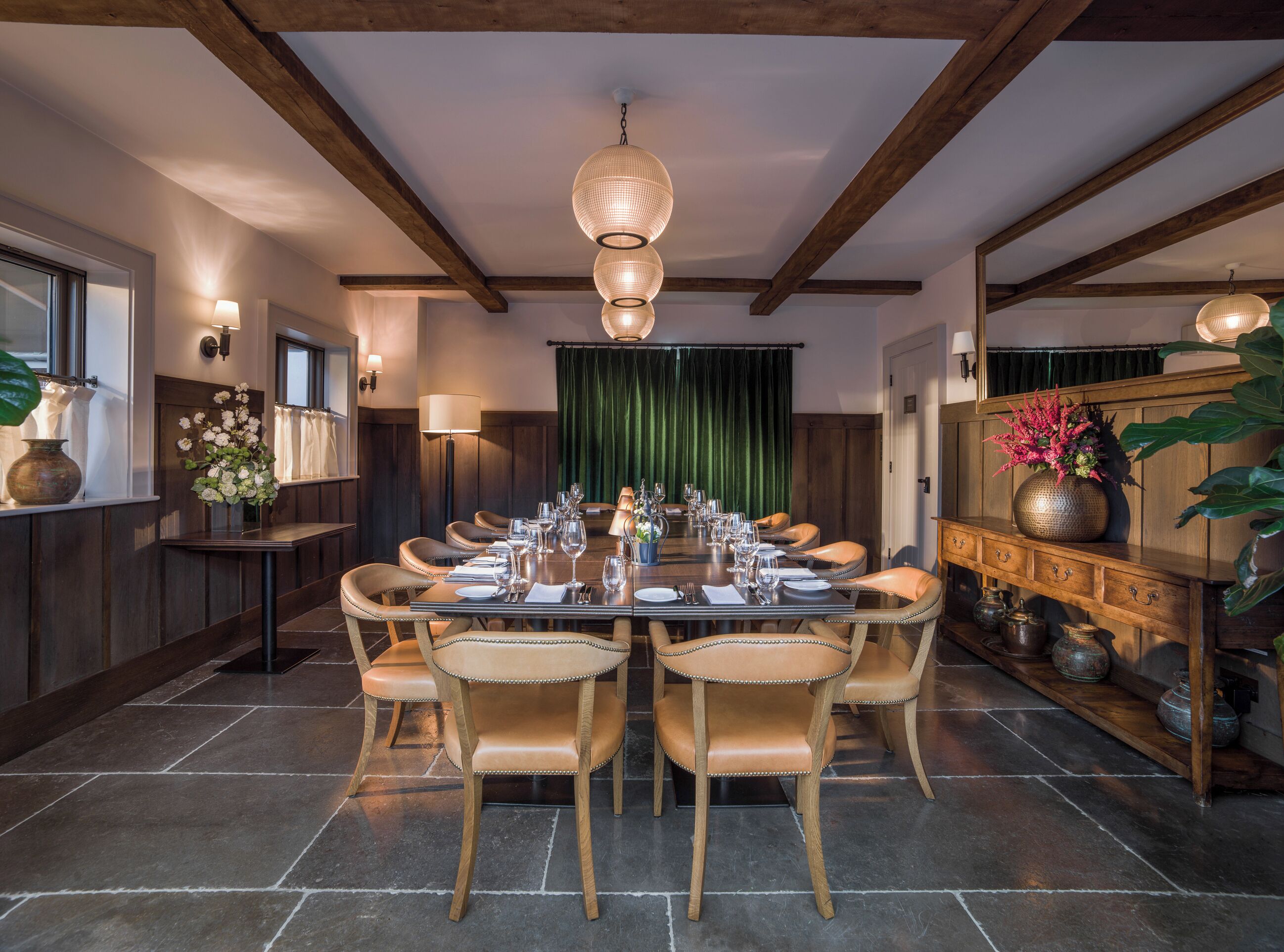 A dining room with a long table set for a meal, wooden beams on the ceiling, and a green curtain in the background.
