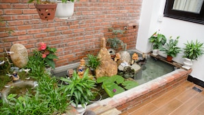 Un pequeño estanque con rocas y plantas, un muro de ladrillo y una ventana con cortina.