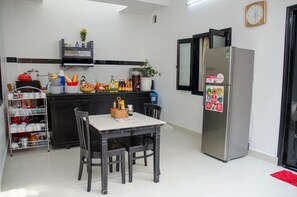 Una cocina con una mesa de comedor, sillas, un refrigerador y varios utensilios de cocina.