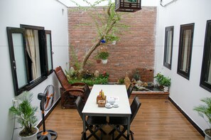 Un patio con una mesa y sillas, rodeado de plantas en macetas y un muro de ladrillo.