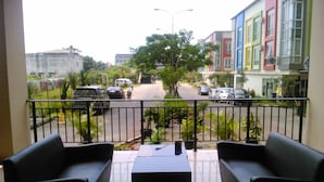 Ein Balkon mit schwarzen Sofas und einem Tisch, mit Blick auf eine Straße mit parkenden Autos und farbenfrohen Gebäuden.