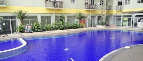 A swimming pool with a blue interior, surrounded by a building with multiple balconies and a yellow lower section.