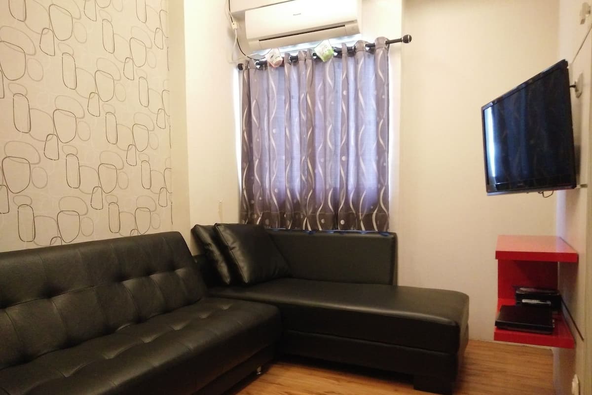 Een moderne woonkamer met een zwarte leren bank, een behangwand, een raam met gordijnen, een wandgemonteerde televisie en een rode entertainmentkast.