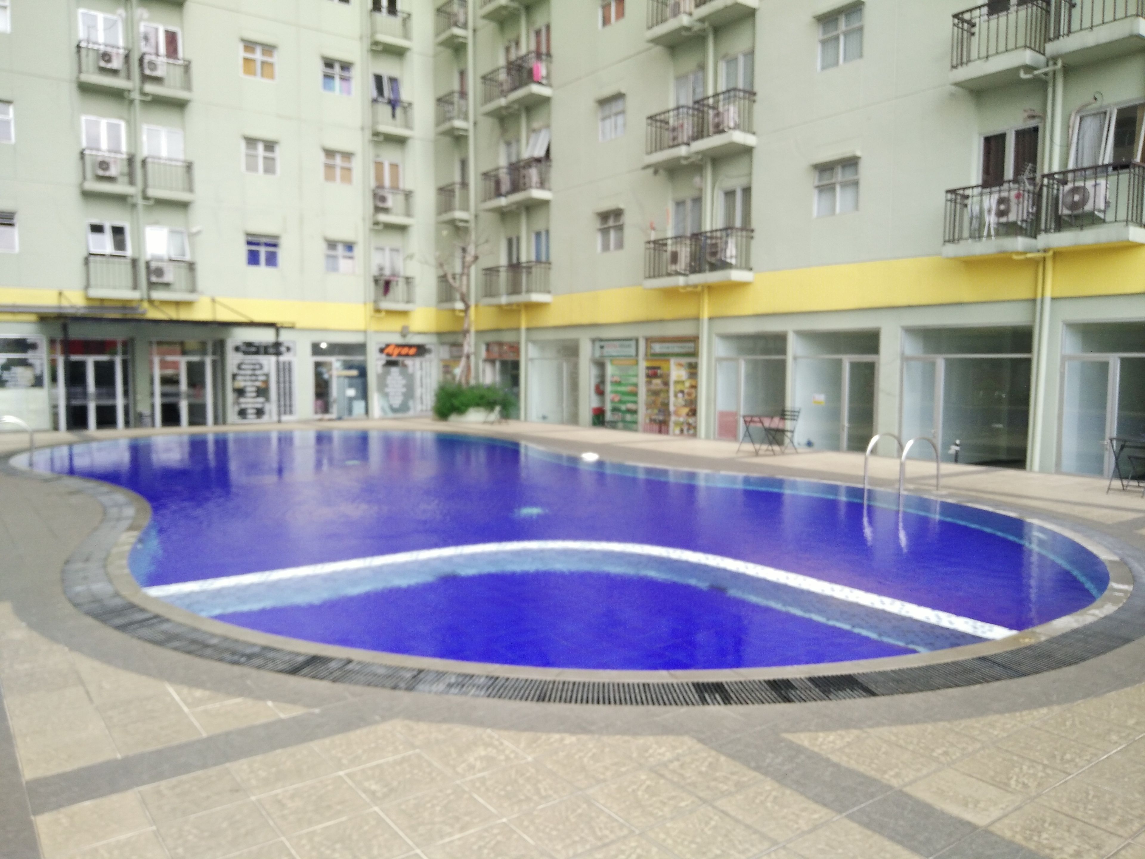 A swimming pool surrounded by a multi-story building with balconies and shops.
