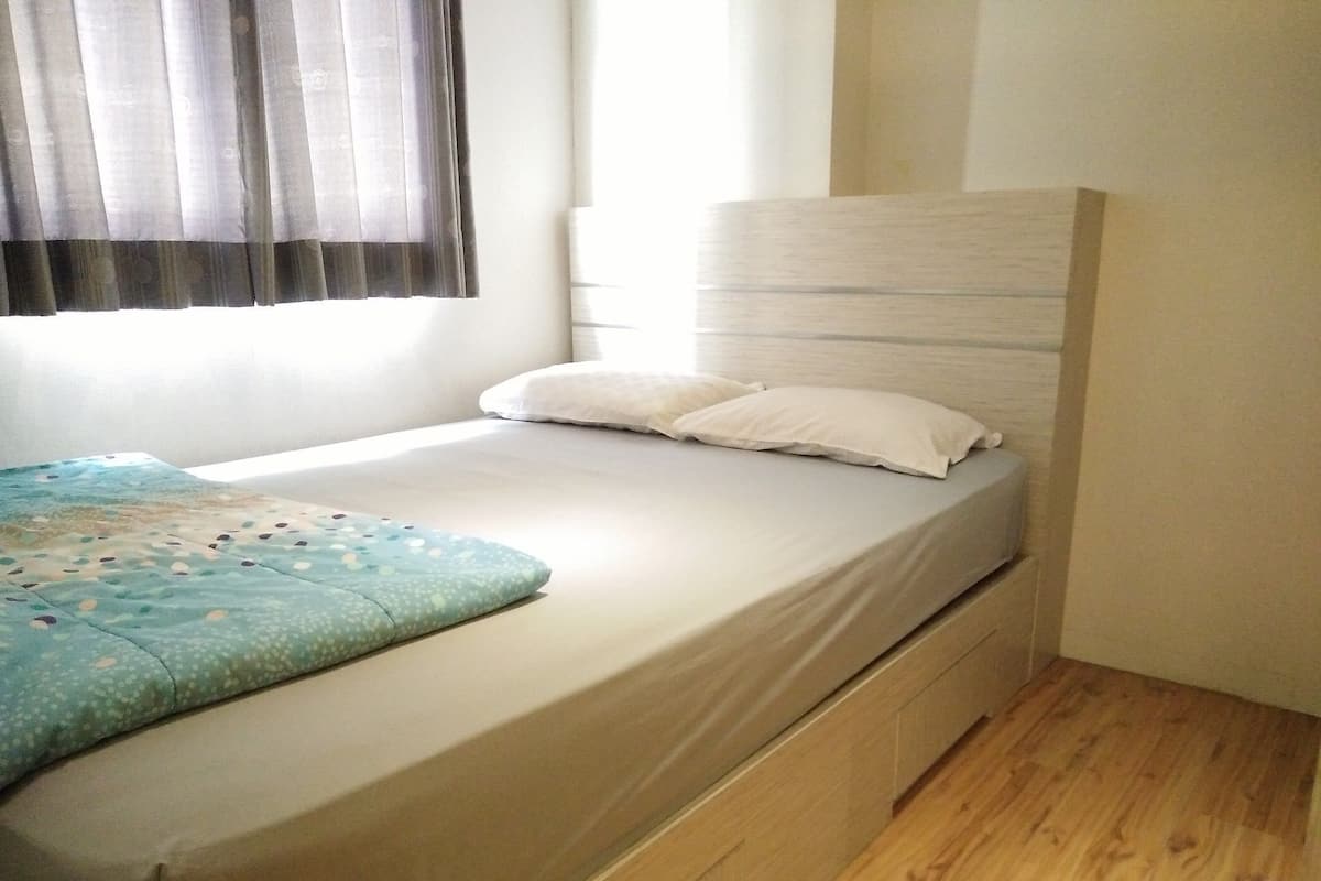 Een enkel bed met een witte matras en hoofdbord, een blauw gebedrukte deken en een kussen.