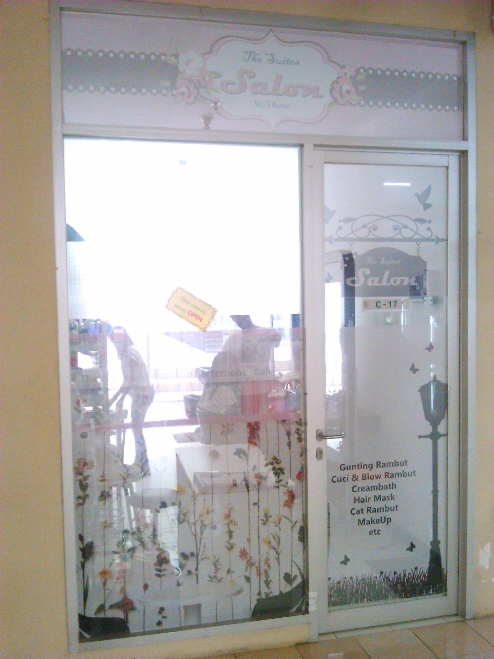 A salon with a floral design on the glass door, a sign indicating it's open, and a list of services like hair mask and cat rambut.