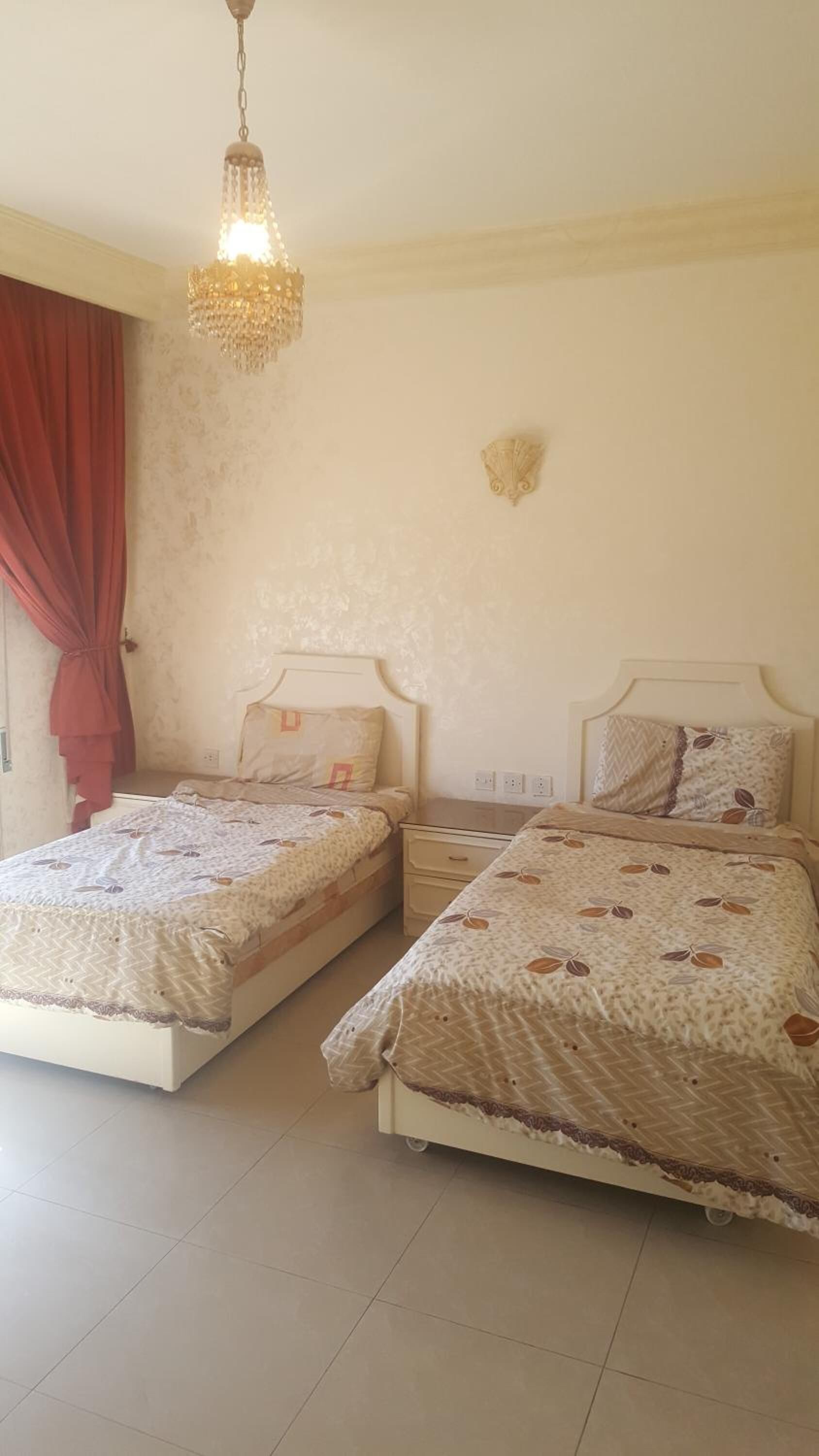 Ein Schlafzimmer mit zwei Betten, einer Kristalllüster, einer Wandleuchte und einem roten Vorhang.