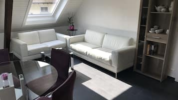 A modern living room with a white sofa, a glass coffee table, and a wooden cabinet with decorative items.