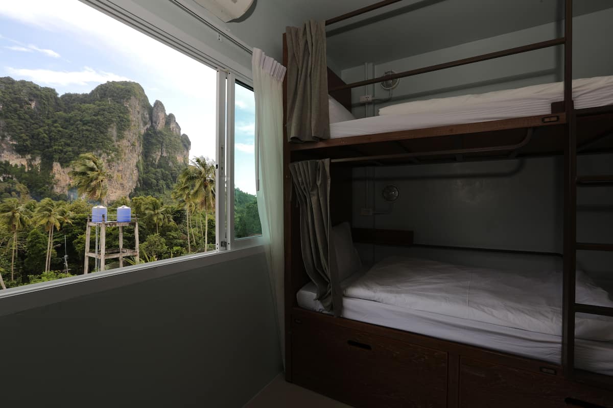 A bunk bed room with a window overlooking a mountainous landscape and palm trees.