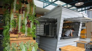 A restaurant with a vertical garden wall, a counter with a person preparing food, and a seating area with tables and stools. - Pop-In Hostel Aonang (Krabi)