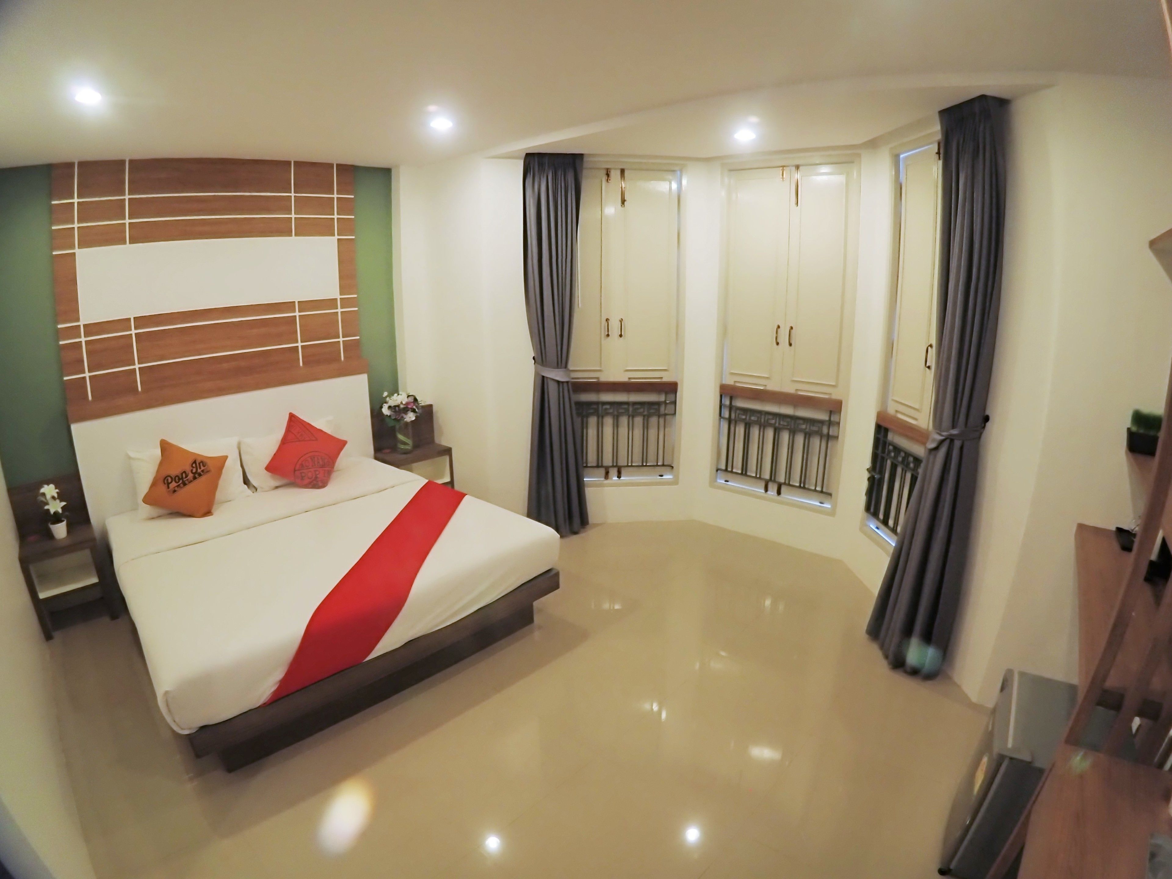 A spacious bedroom with a large bed, a nightstand, a dresser, and a window with curtains.