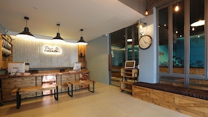 A cozy interior with a wooden reception desk, benches, and a clock on the wall. - Pop-In Hostel Aonang (Krabi)