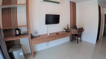 A modern hotel room with a wooden desk, a flat-screen TV, a small plant, and a refrigerator.