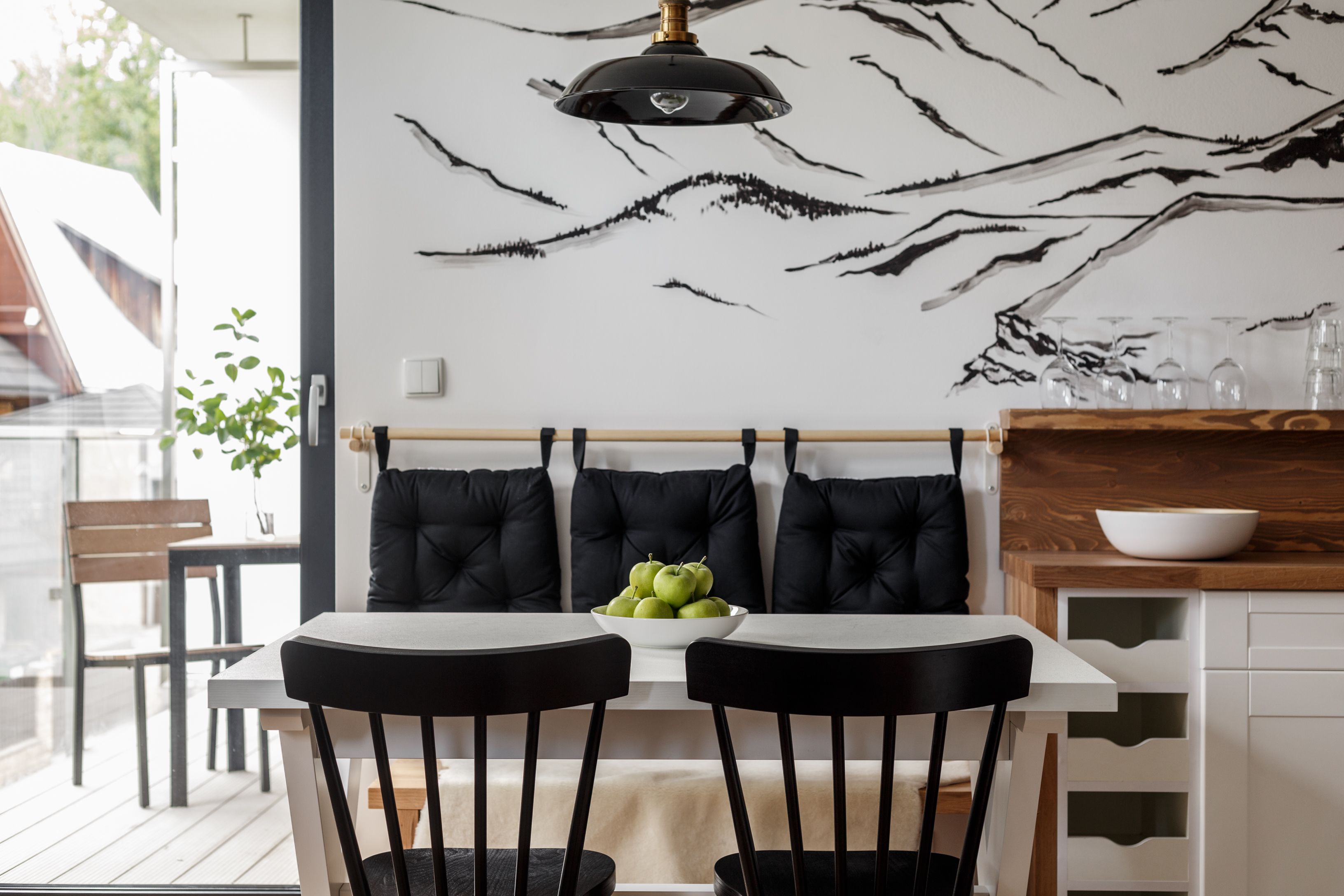A modern dining area with a white table, black chairs, and a bowl of green apples.