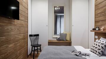 Una habitación compacta con cama, una silla, televisión montada en la pared y una ventana con cortinas.