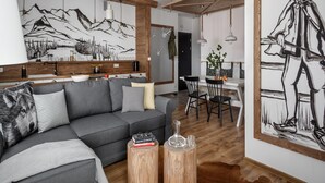 A modern living room with a gray sofa, wooden beams, a dining area with a white table, and a large black and white painting. - Tatrytop Apartamenty Granitica (Zakopane)