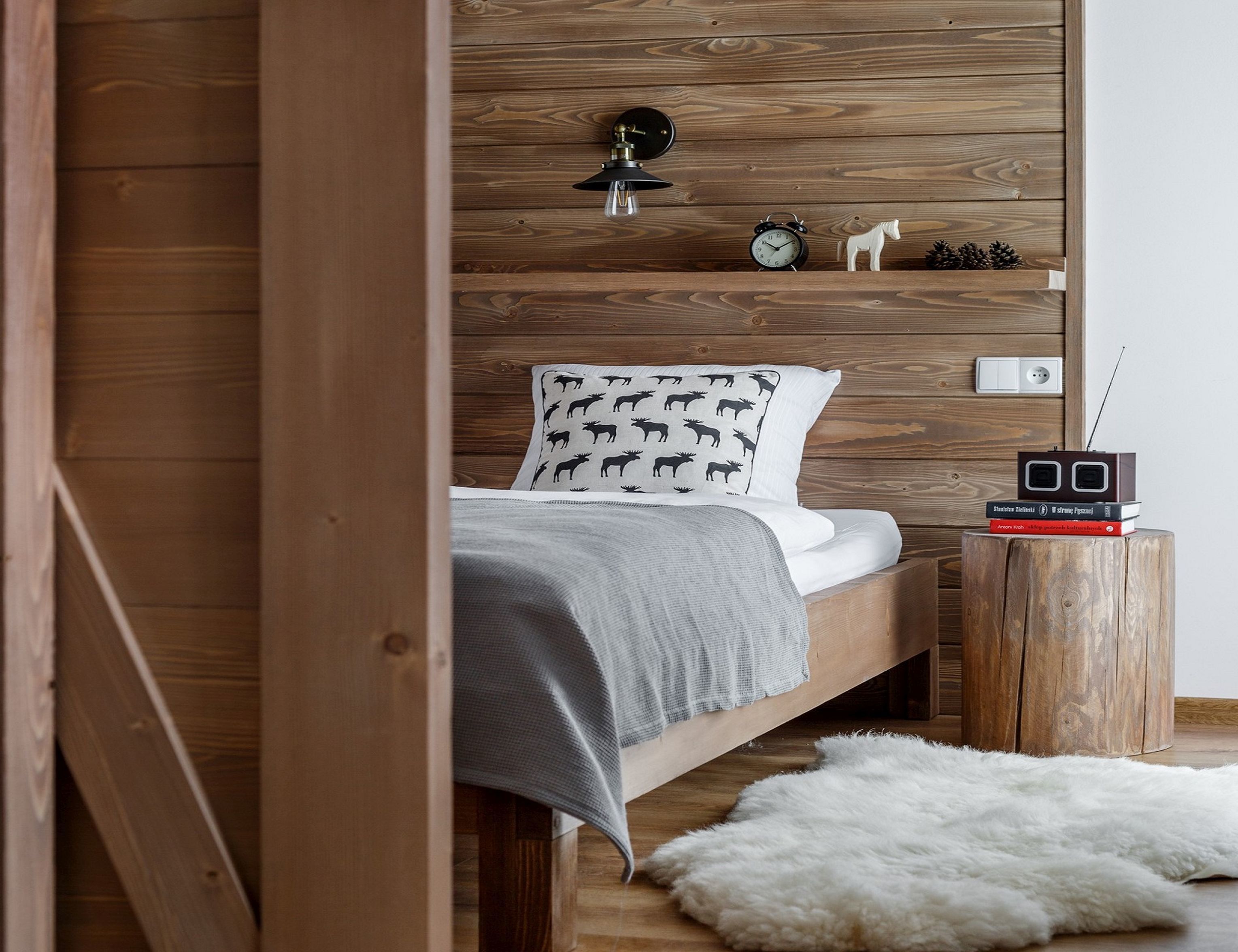 A bedroom with a wooden headboard, a bed with white bedding, a small wooden nightstand with a radio, and a white furry rug.
