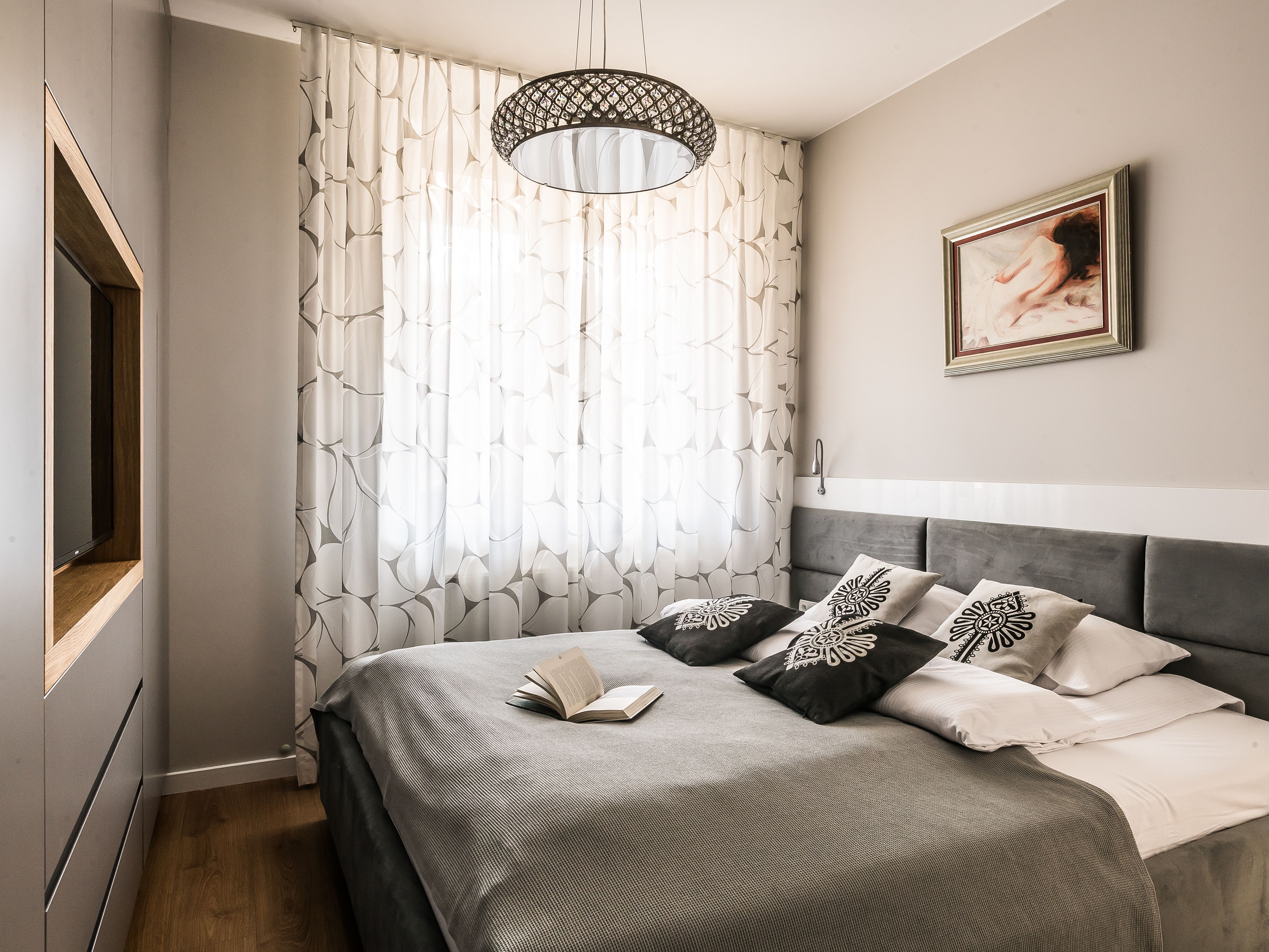 Une chambre à coucher moderne avec un grand lit, une table de chevet, un téléviseur fixé au mur et un luminaire suspendu au plafond.
