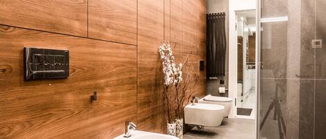 A modern bathroom with wooden paneling, a vanity with a sink, a bidet, and a glass shower enclosure.