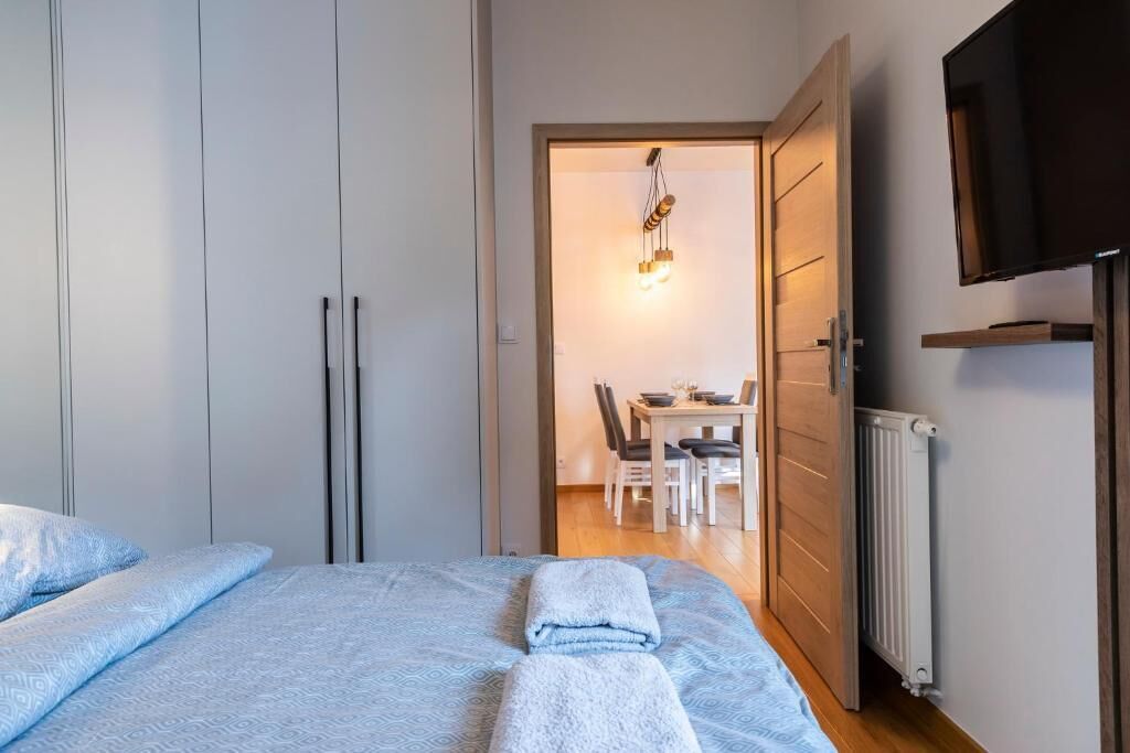 A bedroom with a bed, a wardrobe, a dining area with chairs and a table, and a television mounted on the wall.