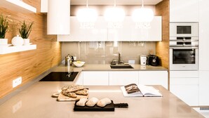 A modern kitchen with a wooden accent wall, a built-in oven, and a countertop with bread and a book. - Tatrytop Apartamenty Granitica (Zakopane)