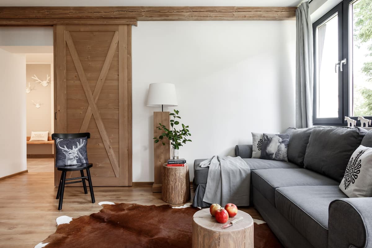 Una sala de estar moderna con un sofá gris, una silla de madera, un tapiz de piel de vaca, una mesita de madera con manzanas y una lámpara.