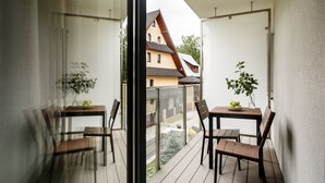 A balcony with a wooden table and chairs, a glass railing, and a view of a house in the background. - Tatrytop Apartamenty Granitica (Zakopane)