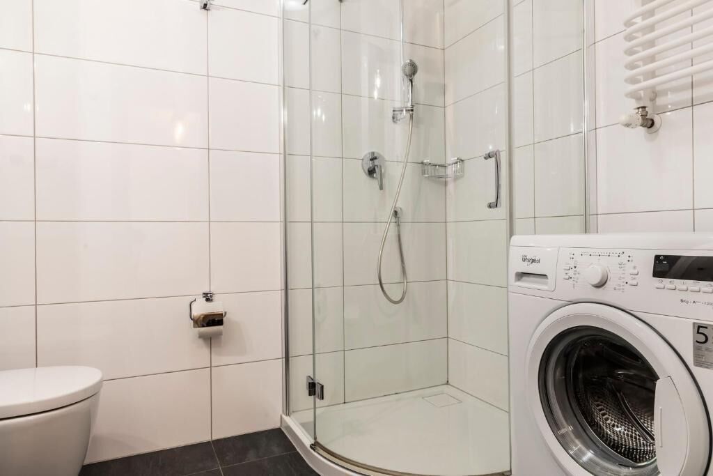 Un baño con ducha de vidrio, inodoro y lavadora de carga frontal.