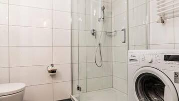 Un baño con ducha de vidrio, inodoro y lavadora de carga frontal.