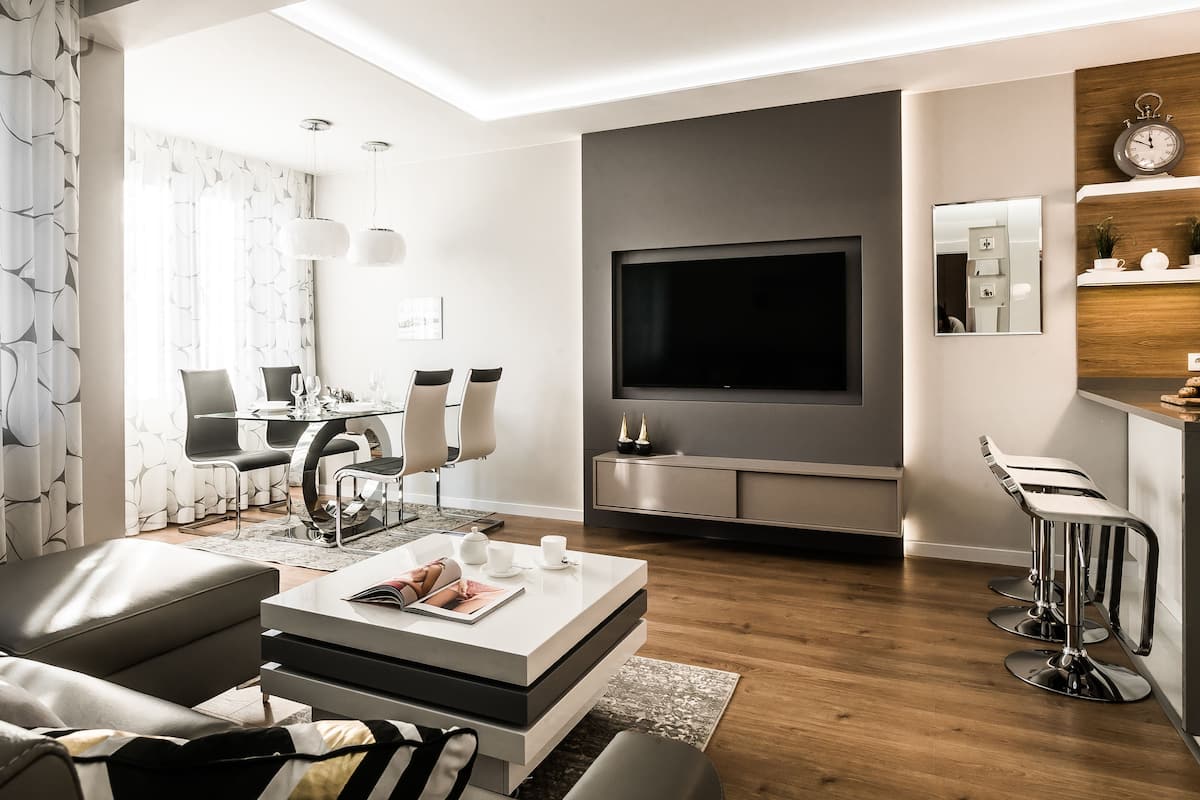 Una sala moderna con un televisor de pantalla plana, un comedor con una mesa de vidrio y una zona de bar con taburetes.