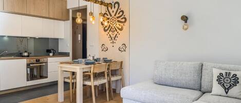 A modern kitchen with wooden cabinets, a dining table with chairs, a grey sofa, and a decorative wall piece.
